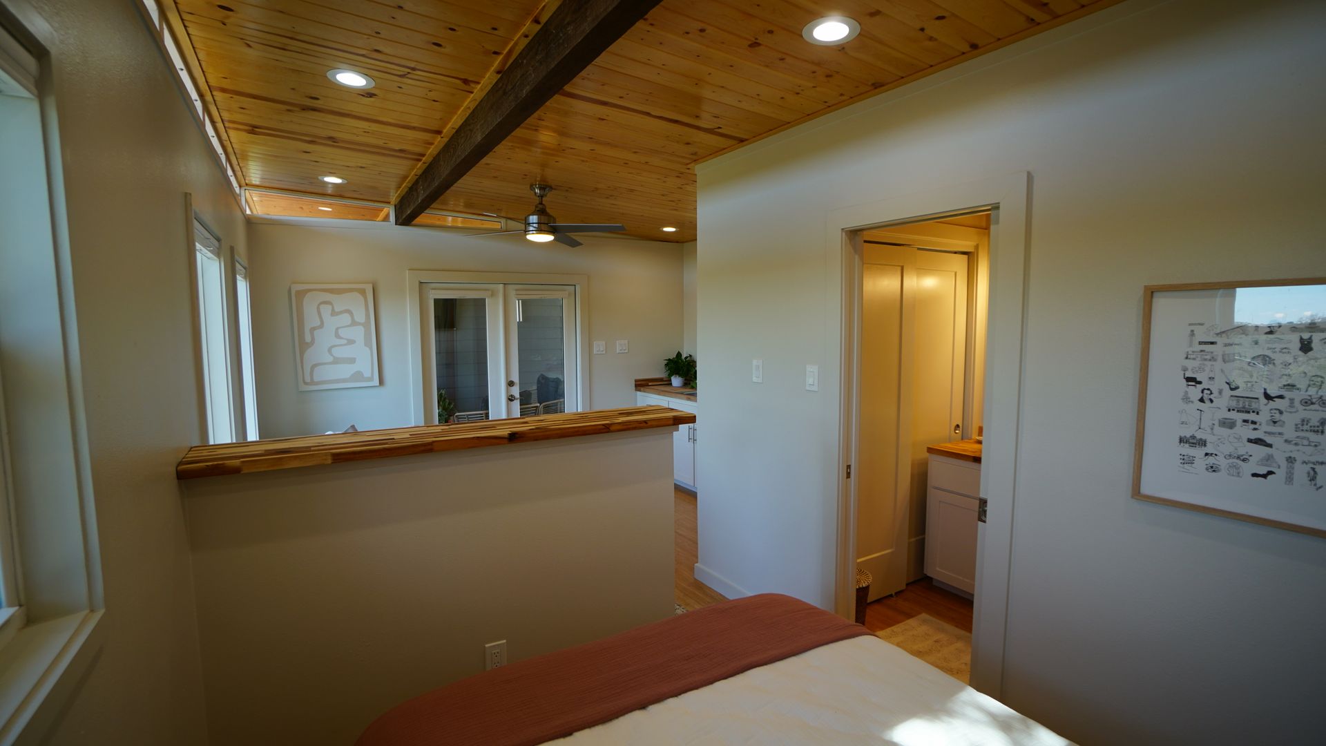 Interior view: bedroom with wood ceiling, partial wall with counter, open to kitchen and doorway to a bathroom.