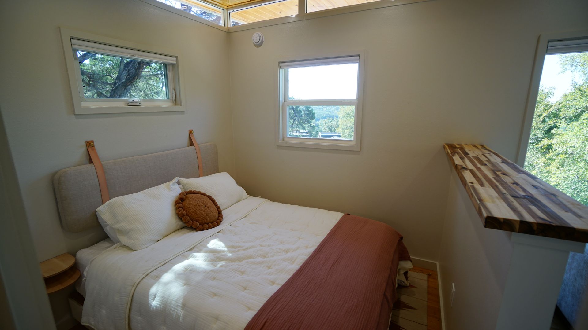 Bedroom with bed, pillows, window, and small table. Beige walls, wood accents, and natural light.