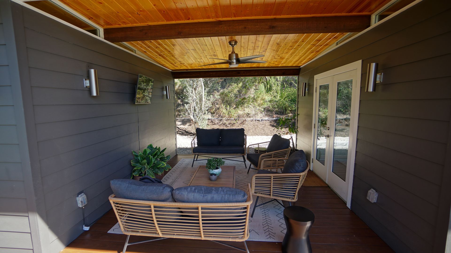 Outdoor patio with gray walls, wood ceiling, and furniture.