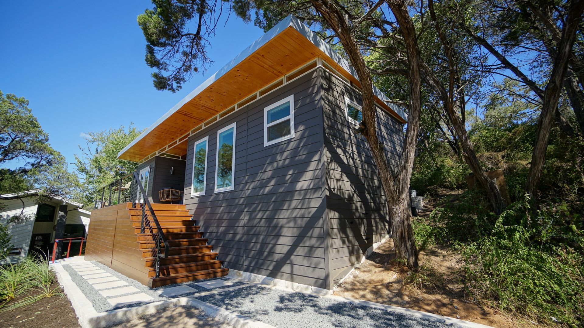 Gray cabin with a wooden stair entrance; trees and blue sky.