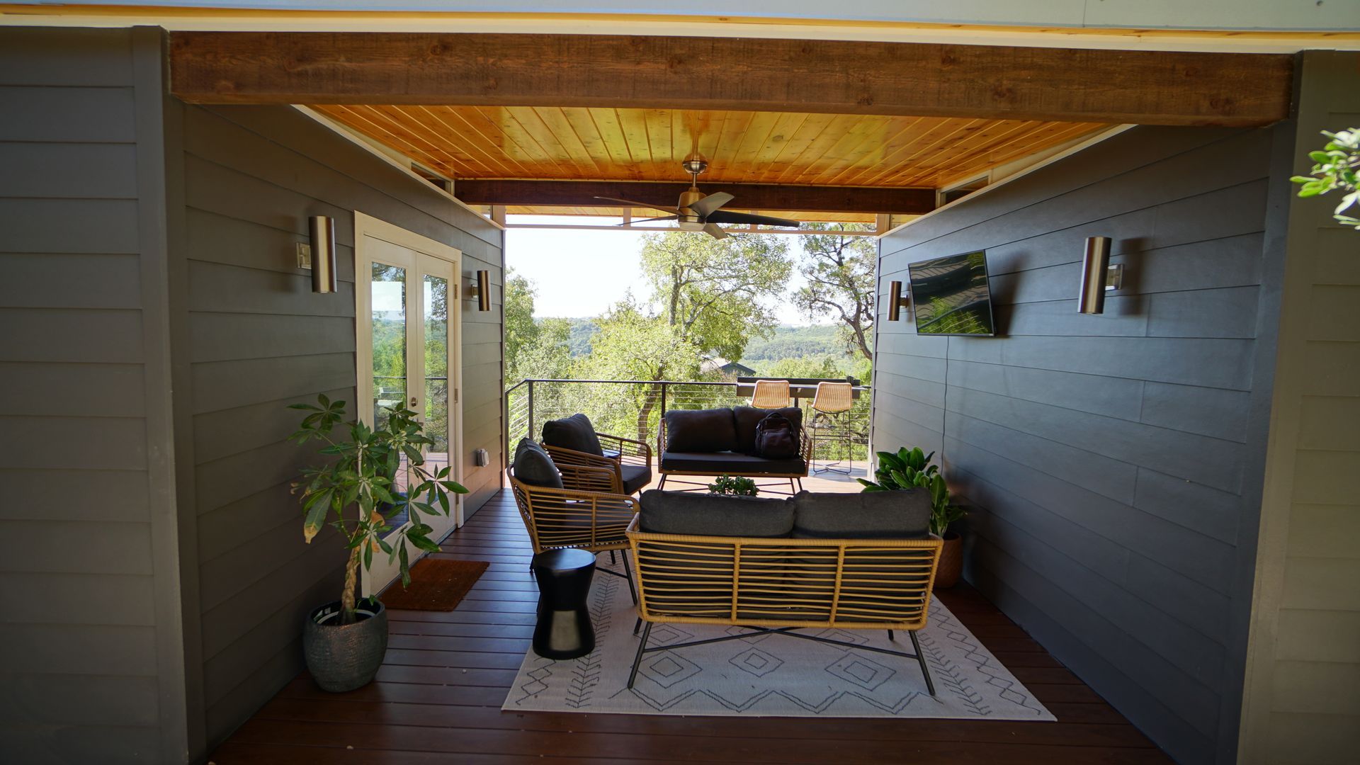 Outdoor patio with seating, open to a view. Features grey walls, wooden ceiling, and a rug.