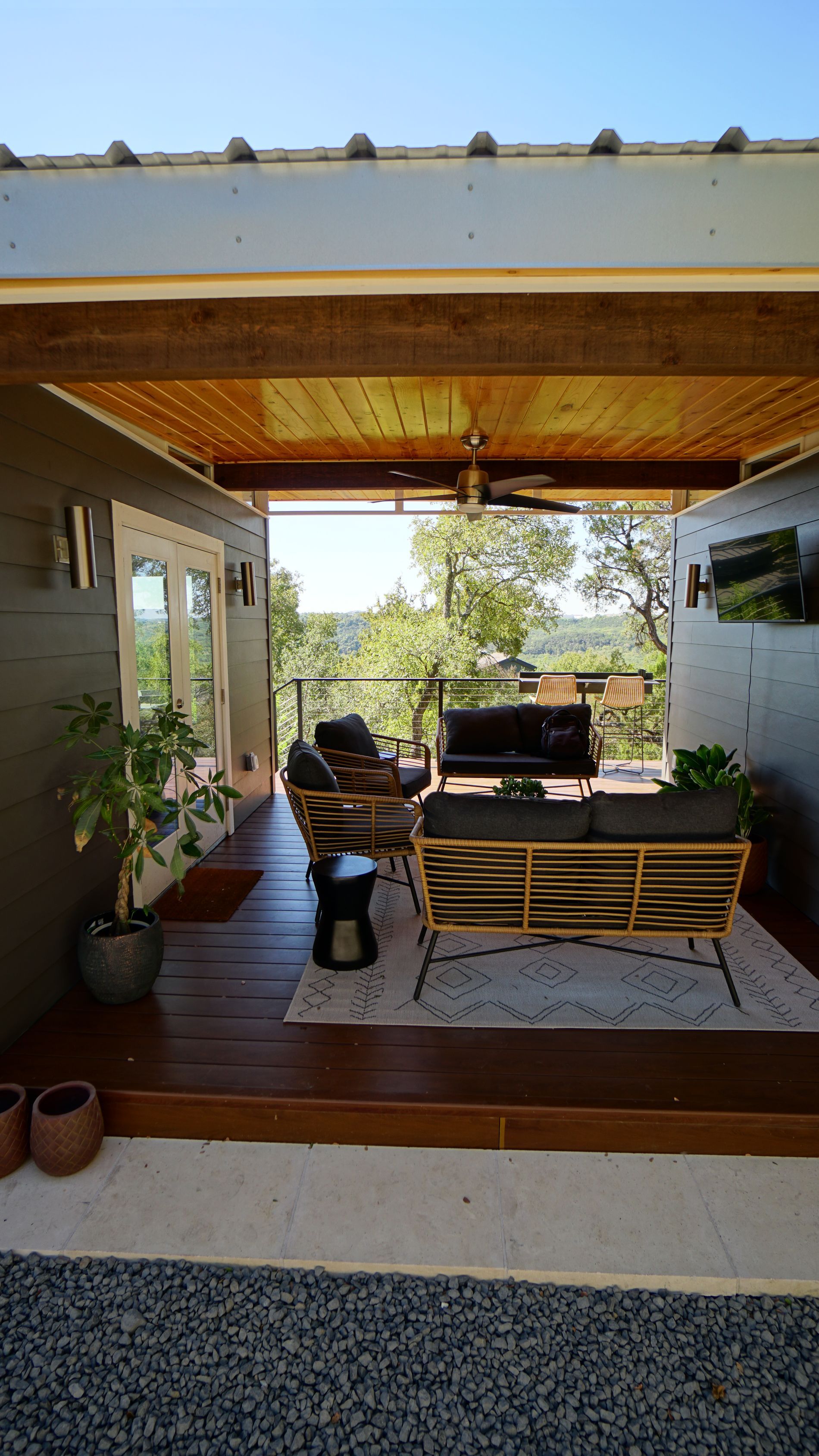 Outdoor seating area with couches, rug, and view of trees. Covered by wooden beams.