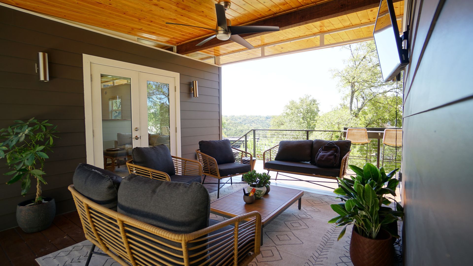 Outdoor patio with seating, wooden ceiling, and view of trees.