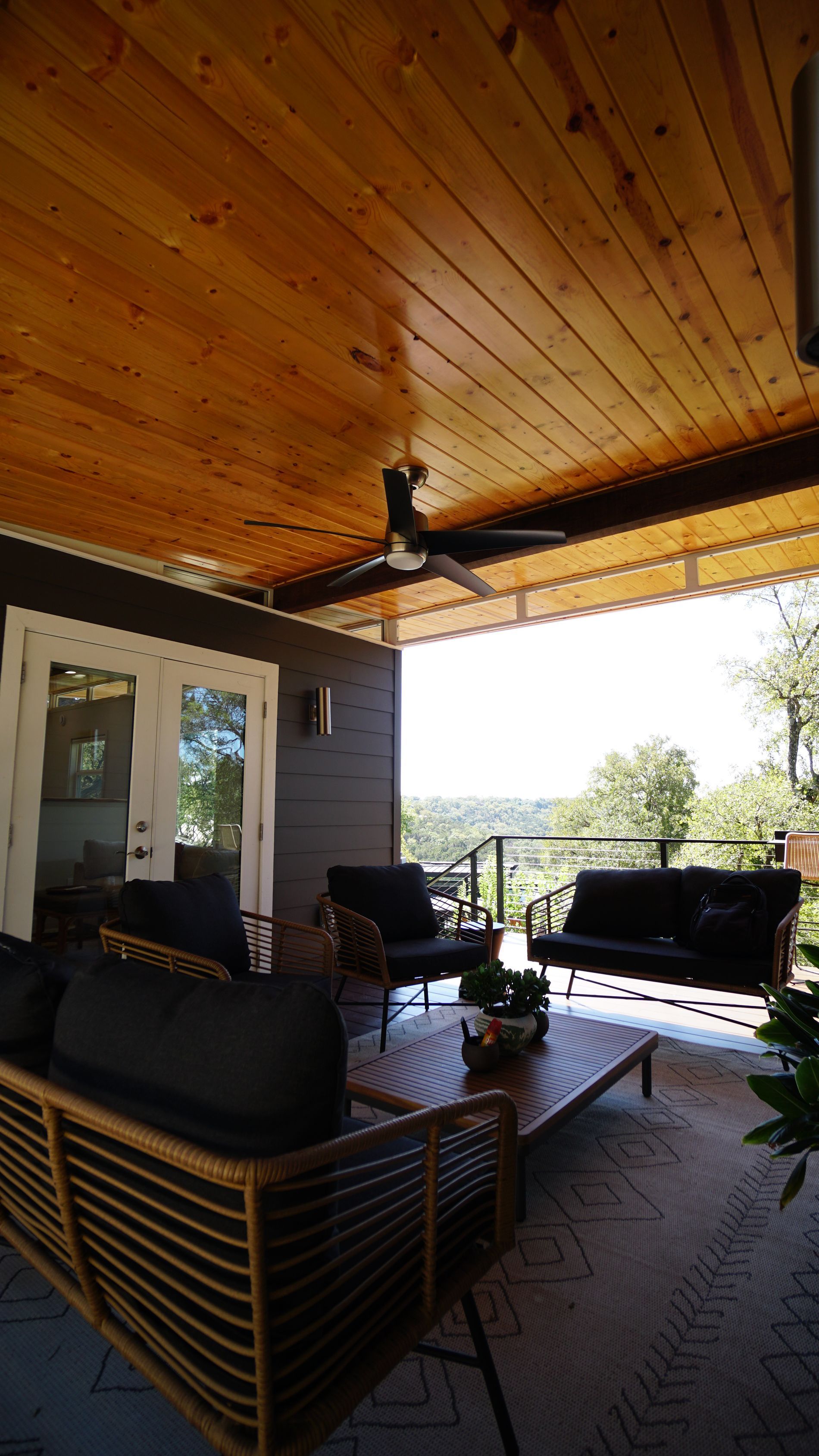 Covered patio with wood ceiling, dark furniture, and a view of trees.