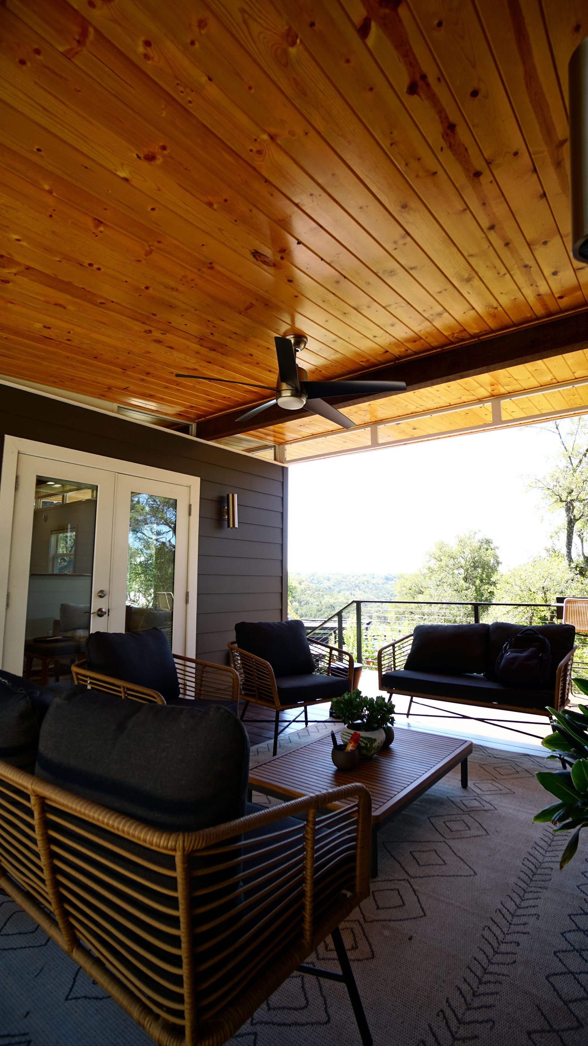 Patio with brown wooden ceiling, dark furniture, and a view of trees.