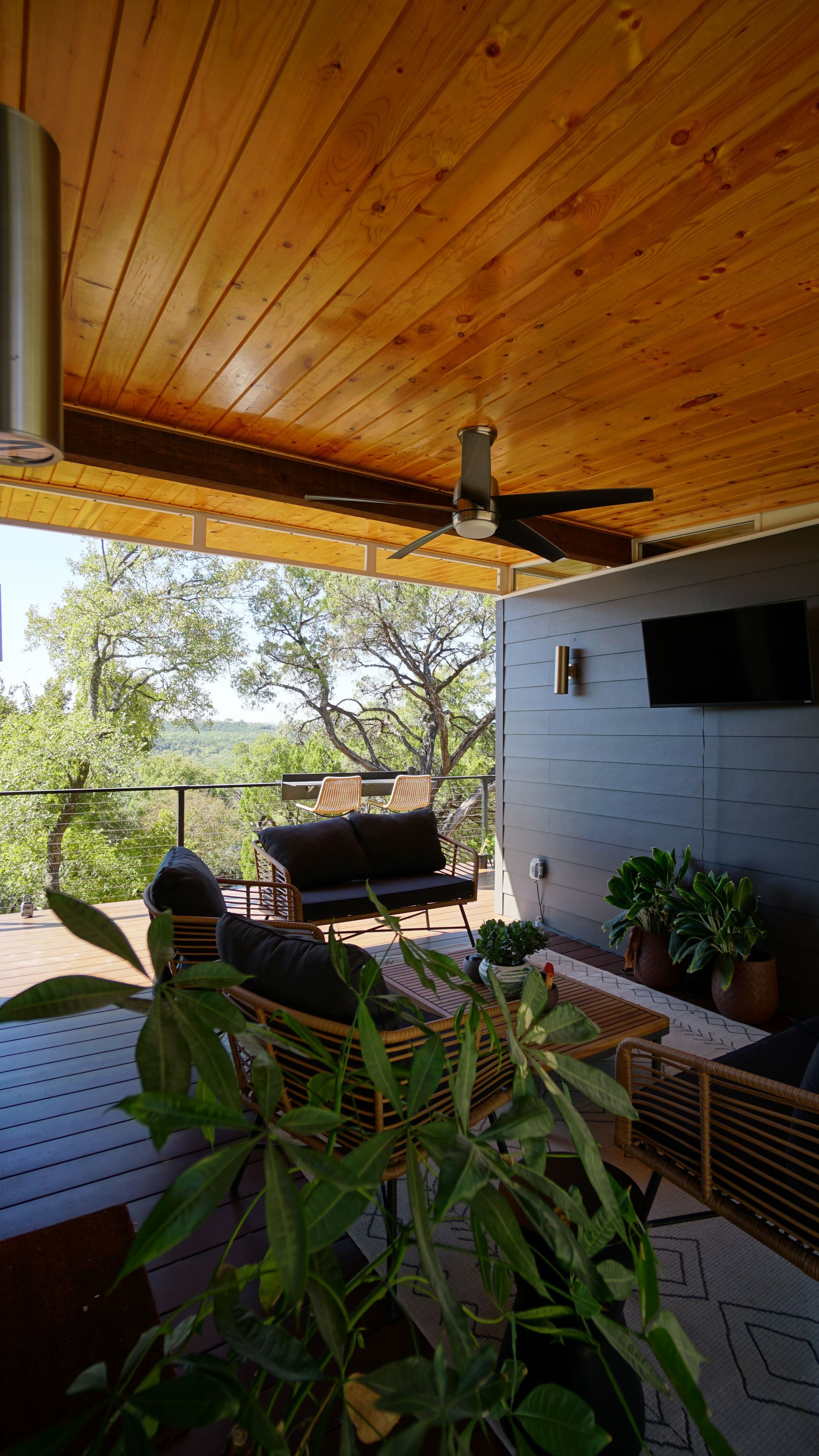 Outdoor patio with wooden ceiling, a ceiling fan, and a view of trees.