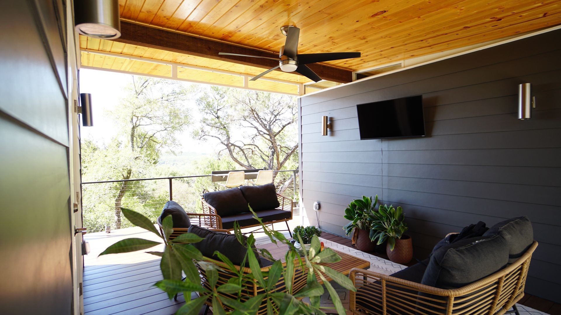 Outdoor patio with dark gray walls, wooden ceiling, seating, and a mounted TV.