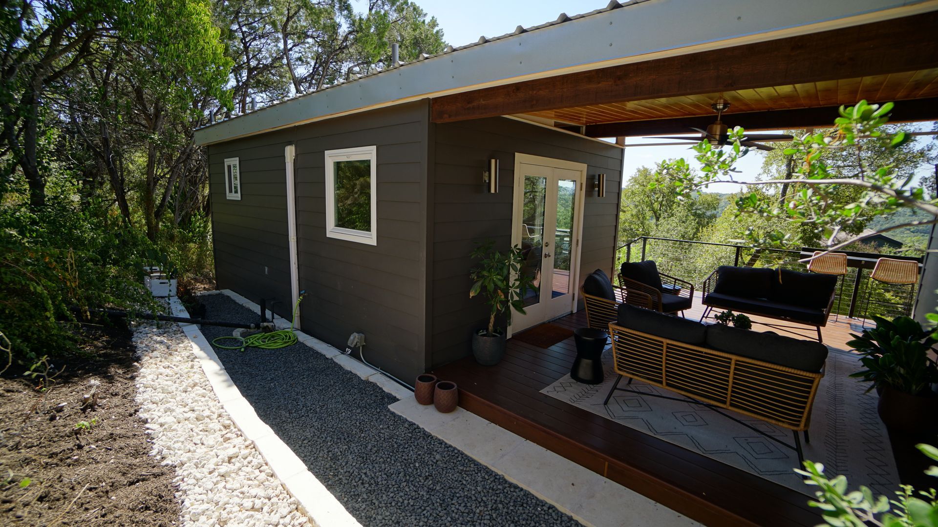Dark gray backyard office with a covered patio and gravel pathway.