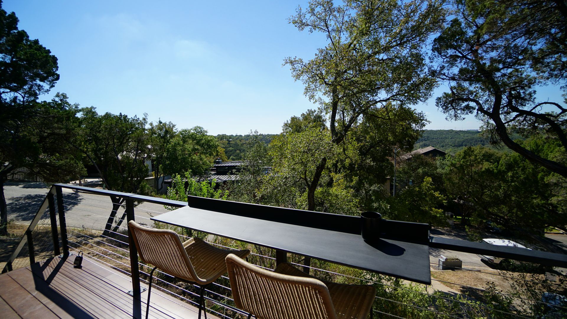 Outdoor patio with chairs and a black table overlooking trees and a distant landscape under a blue sky.