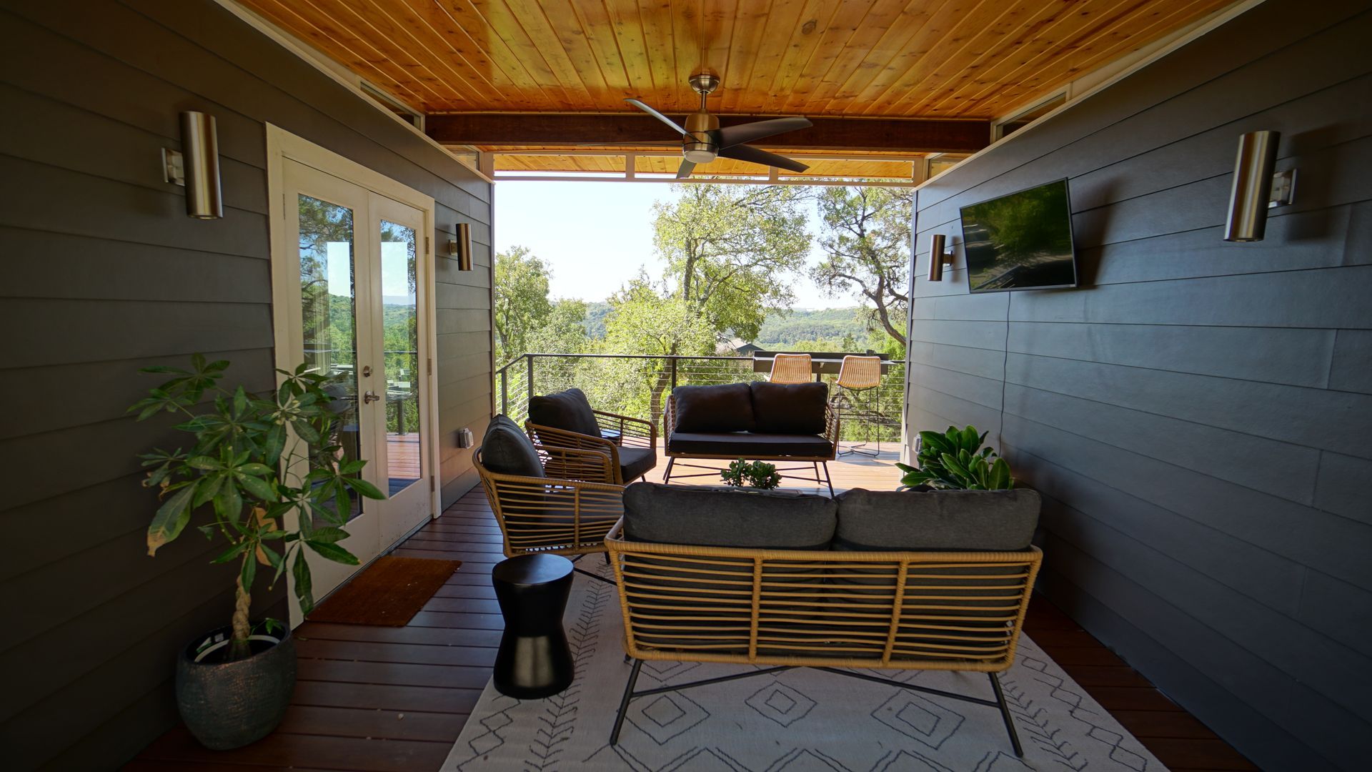 Outdoor deck with seating, mountain view. Gray walls, wood ceiling, potted plants, and a rug.