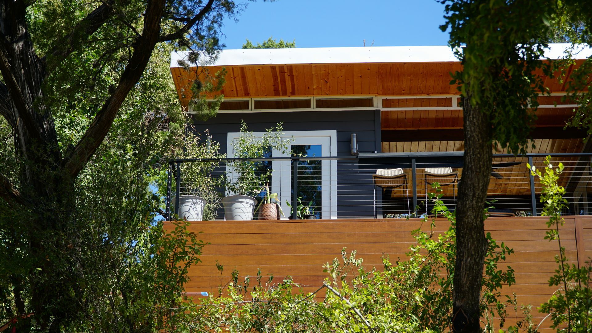 Modern house exterior with wooden deck and trees.