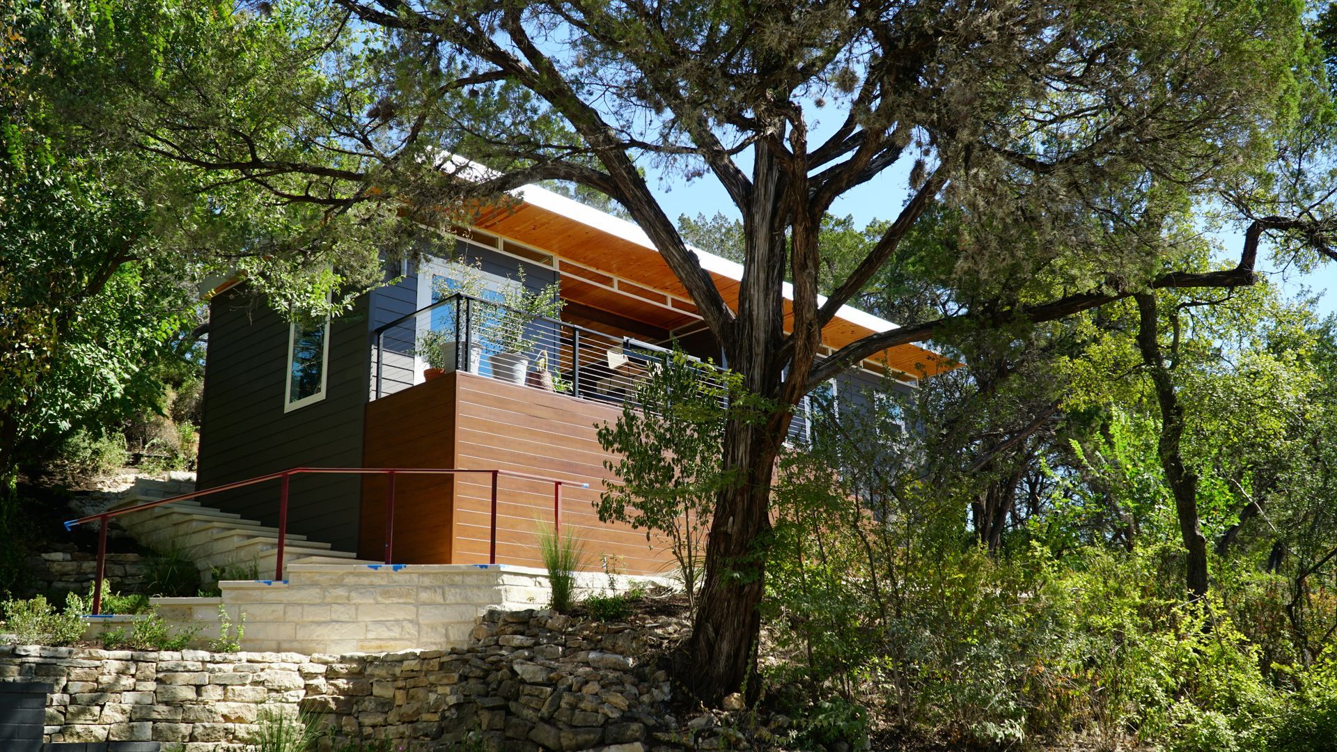 Modern house nestled among trees, with brick, brown siding, and a wooden overhang.