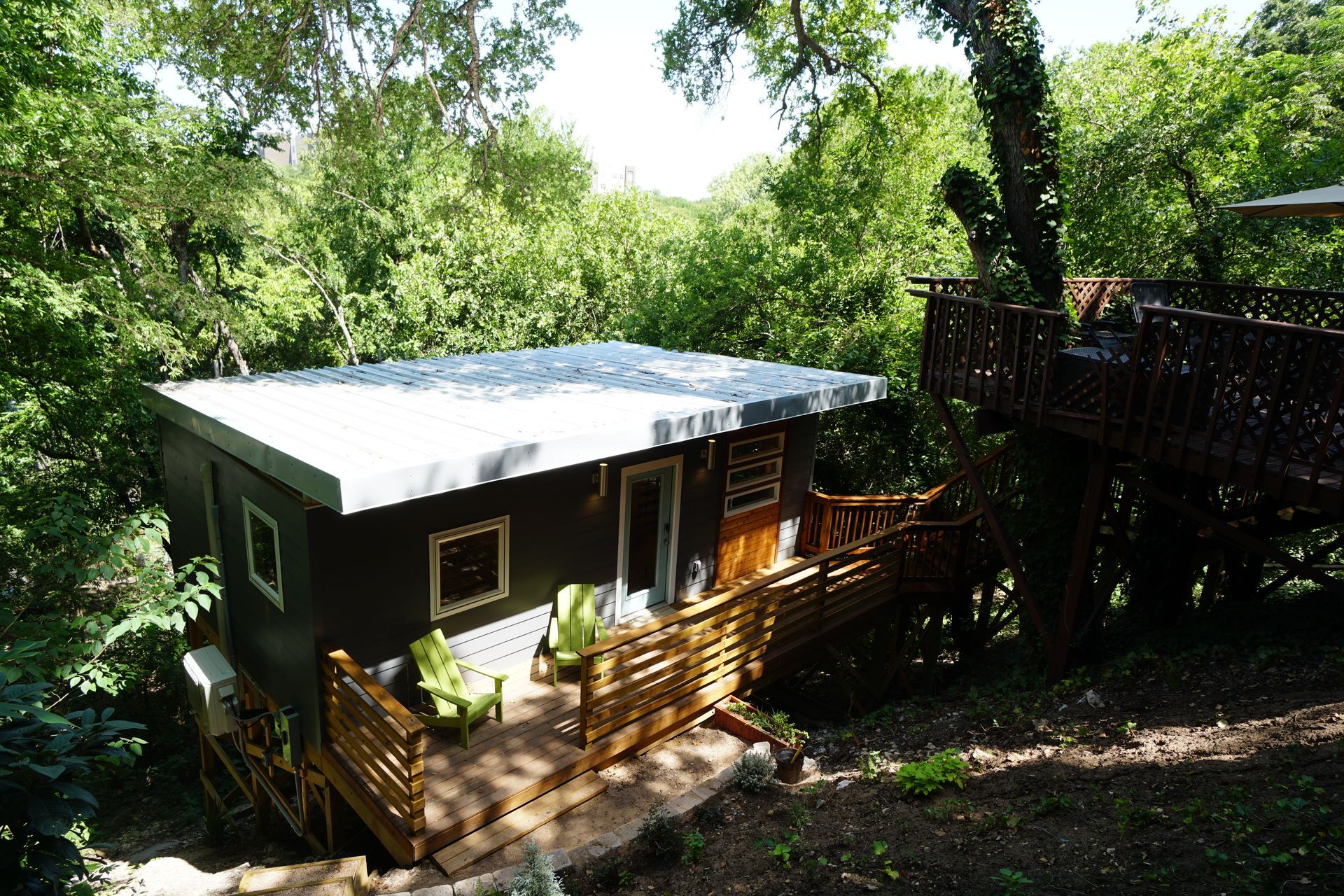 Cabin with a porch and metal roof in a wooded area, with a wooden deck visible.