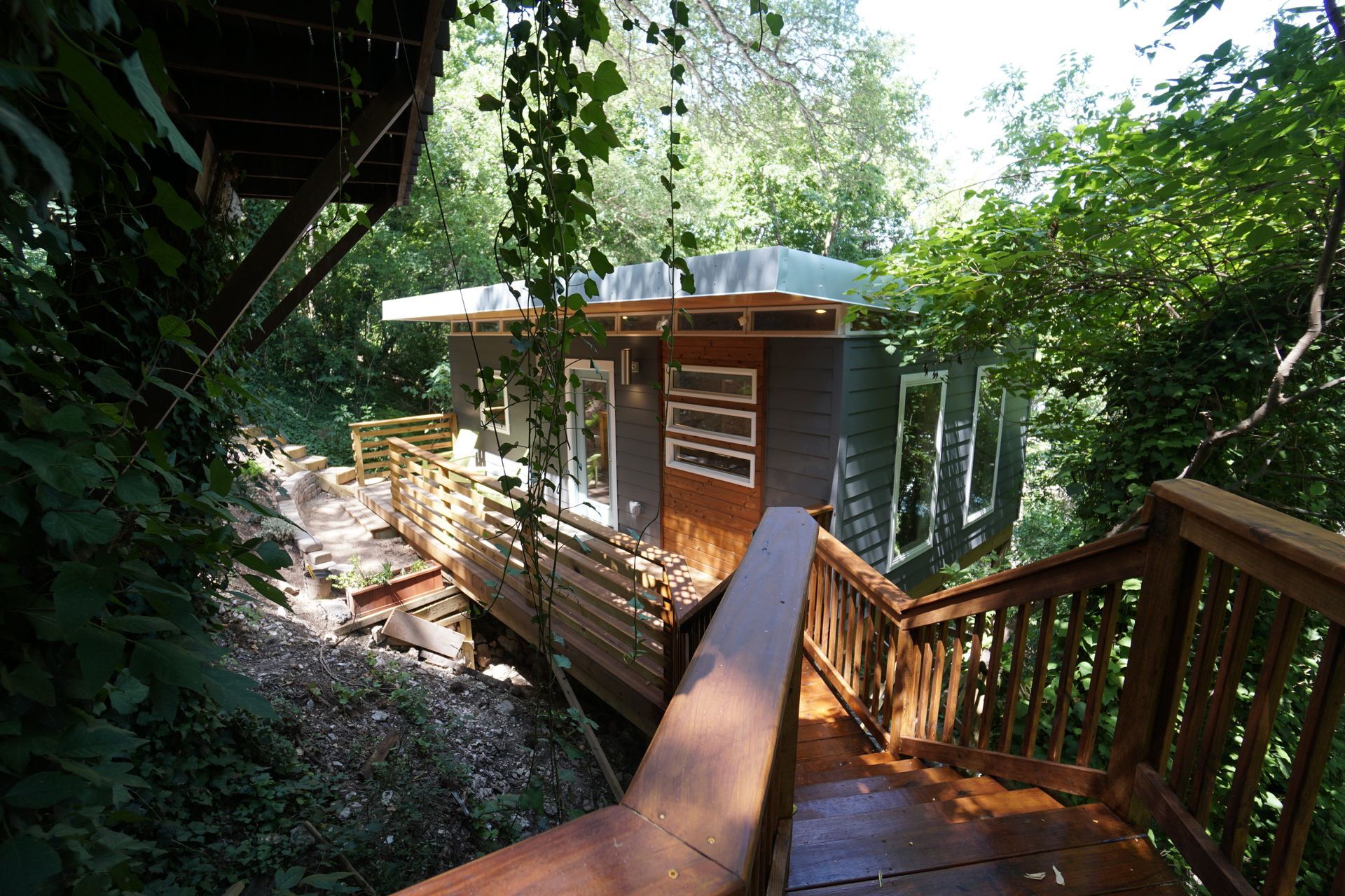 Wooden house nestled in a green forest, accessed by stairs and a walkway.