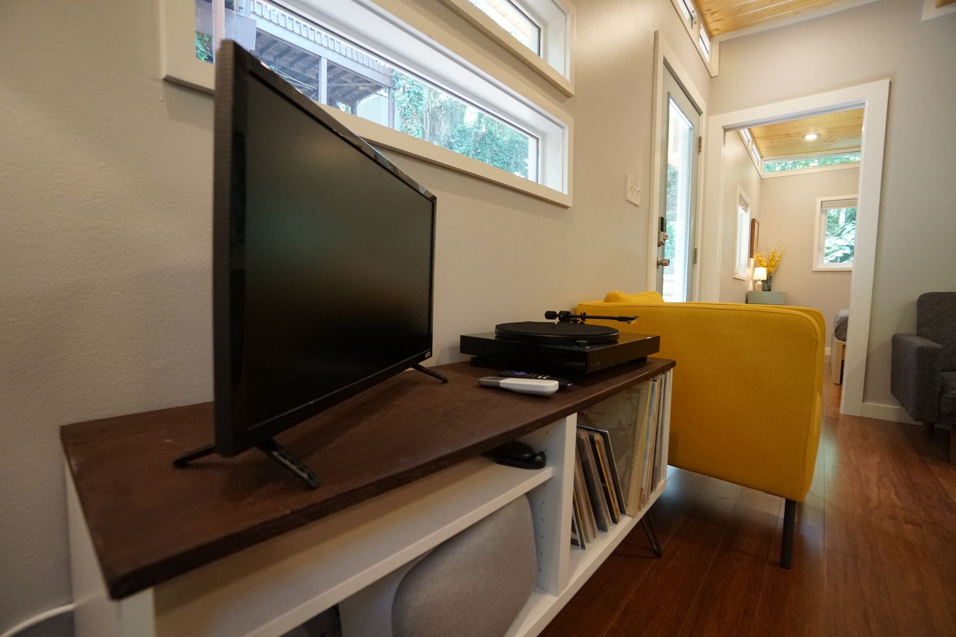 Living room in a tiny house with TV on a white and brown console, yellow chair.