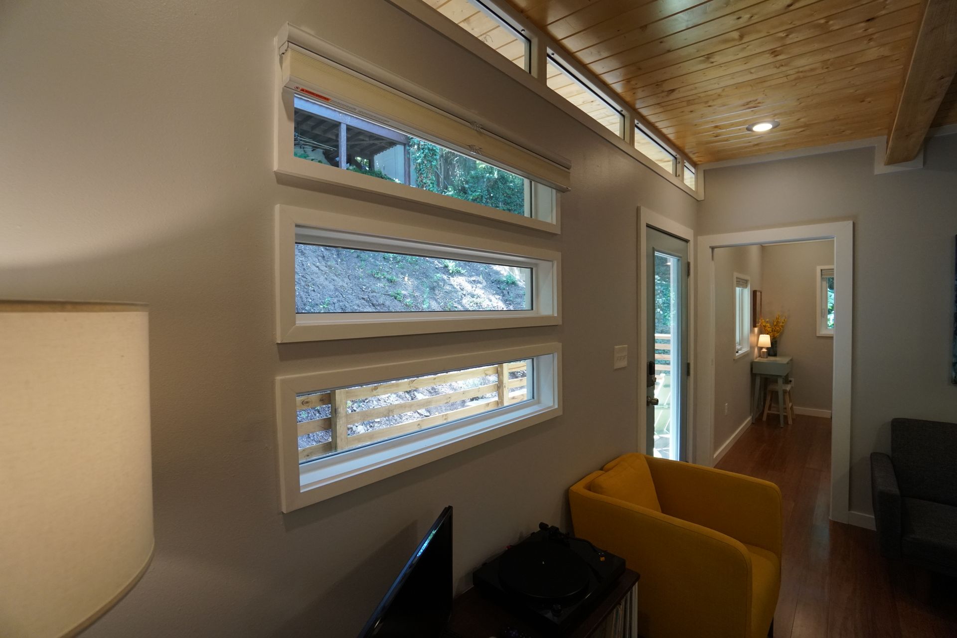 Interior with three rectangular windows, yellow chair, and wooden ceiling.