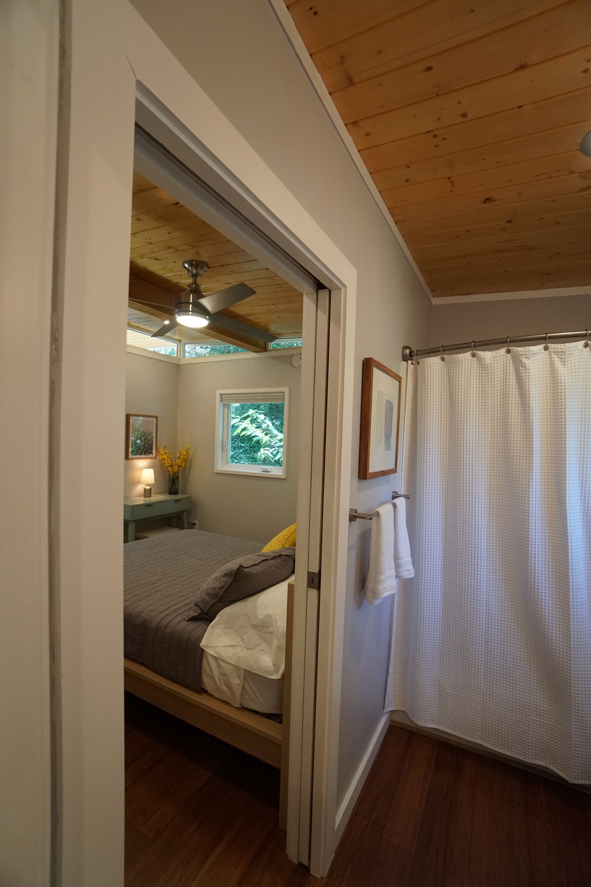 Bedroom doorway leads to a bedroom. Bed, window, artwork, and a ceiling fan are visible.