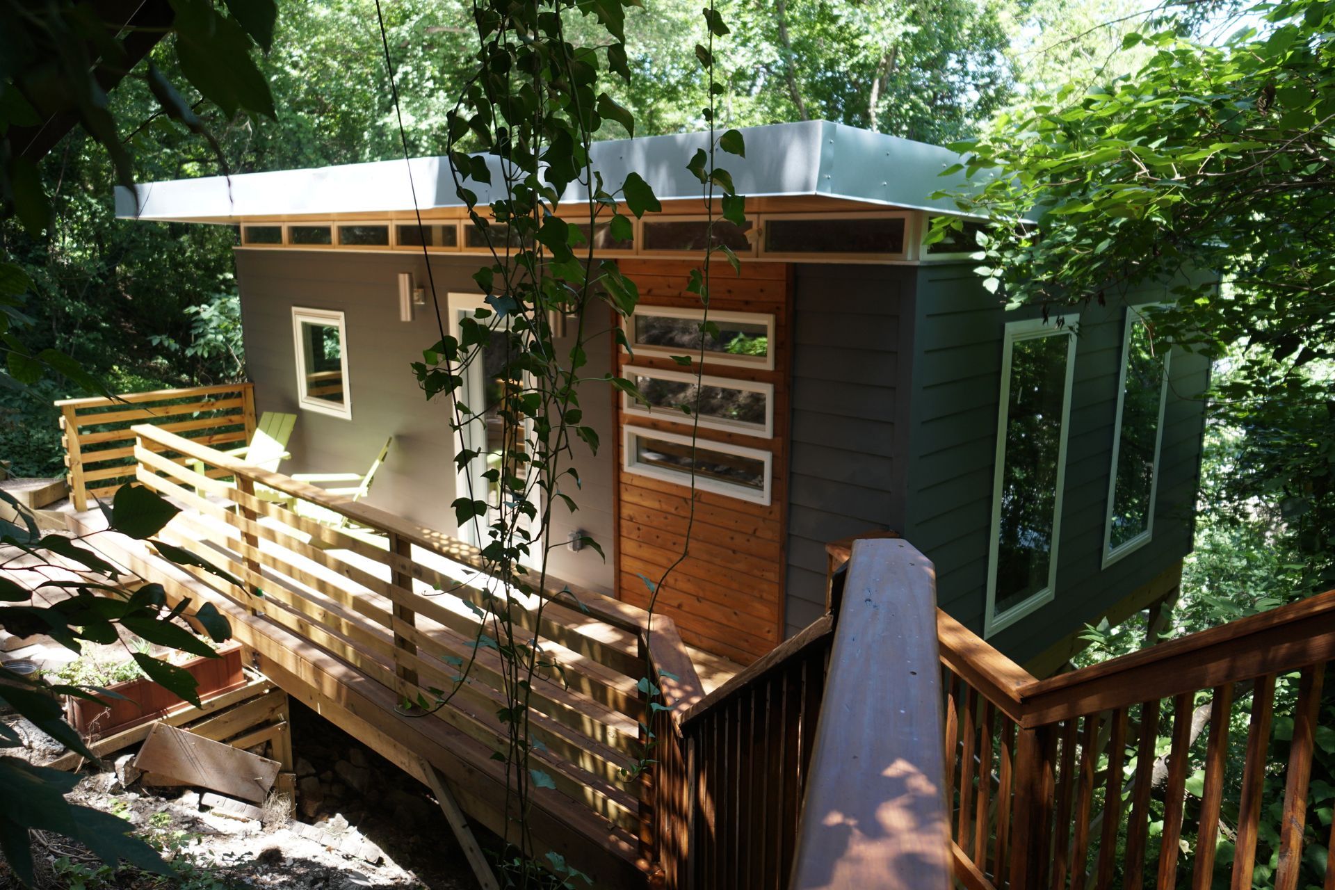 Modern wooden cabin nestled in lush green trees with a wraparound deck.