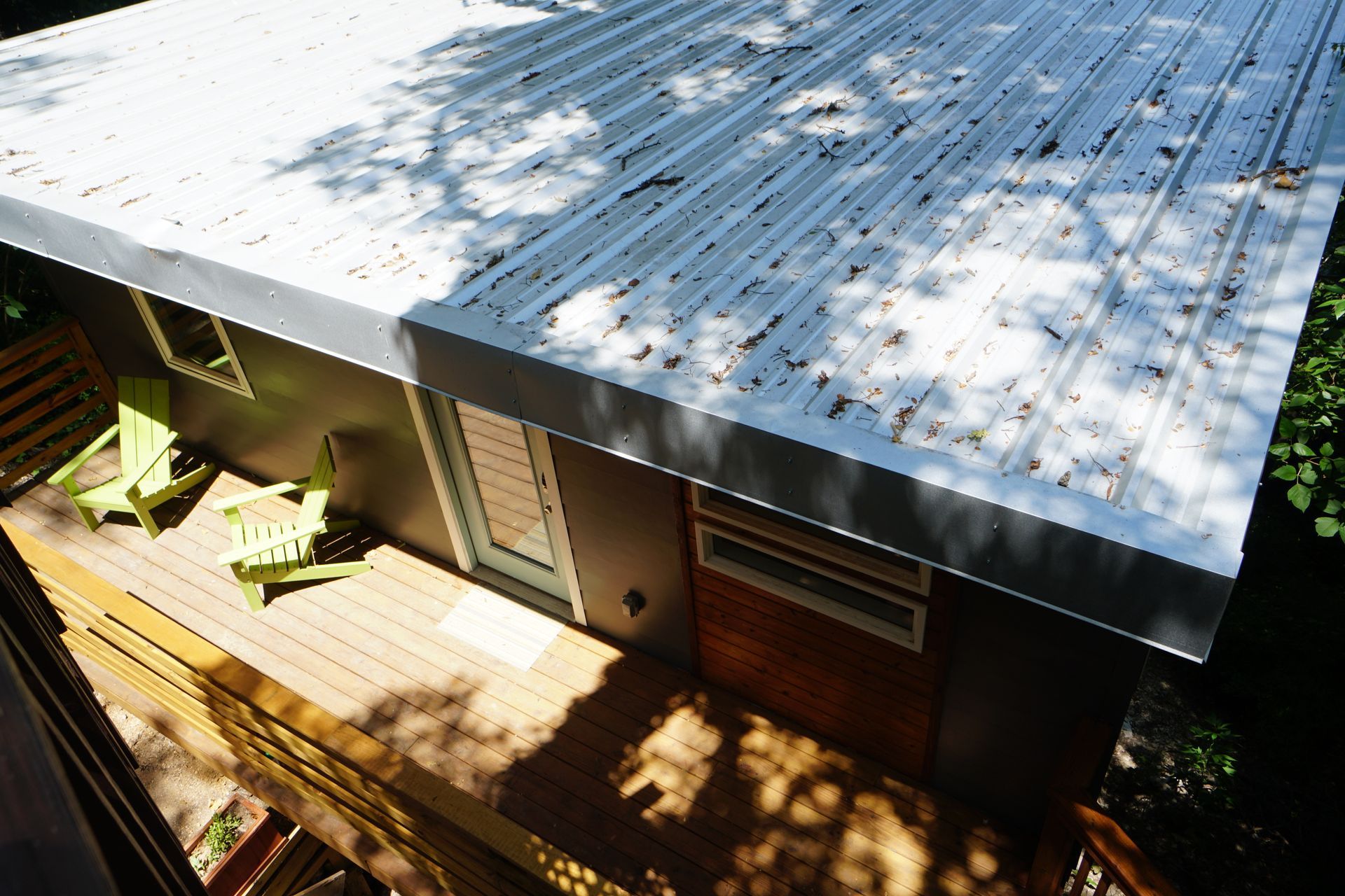 Elevated view of a modern cabin with a metal roof and wooden deck; two green chairs sit on the deck.