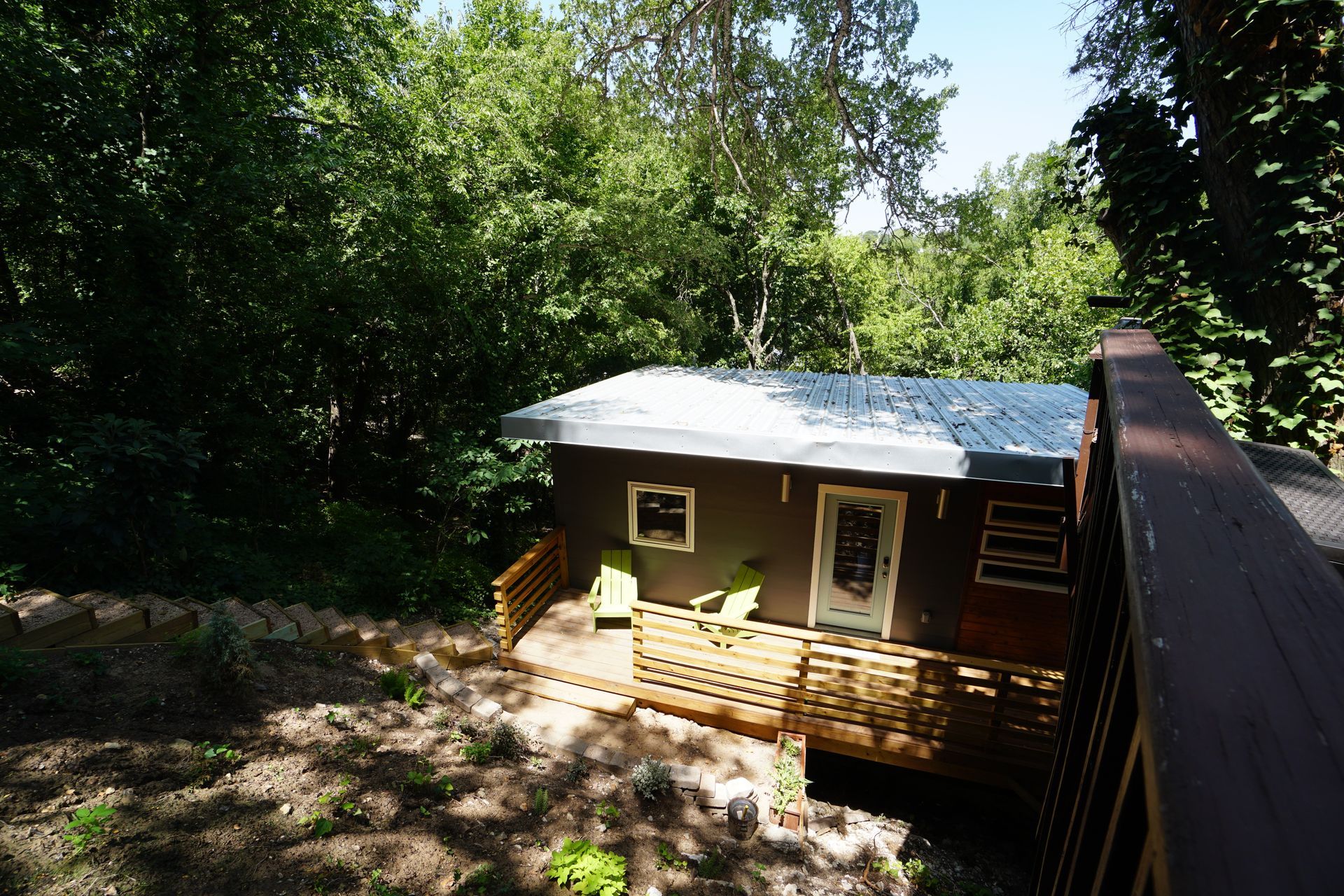 Small brown cabin with wooden deck surrounded by trees.