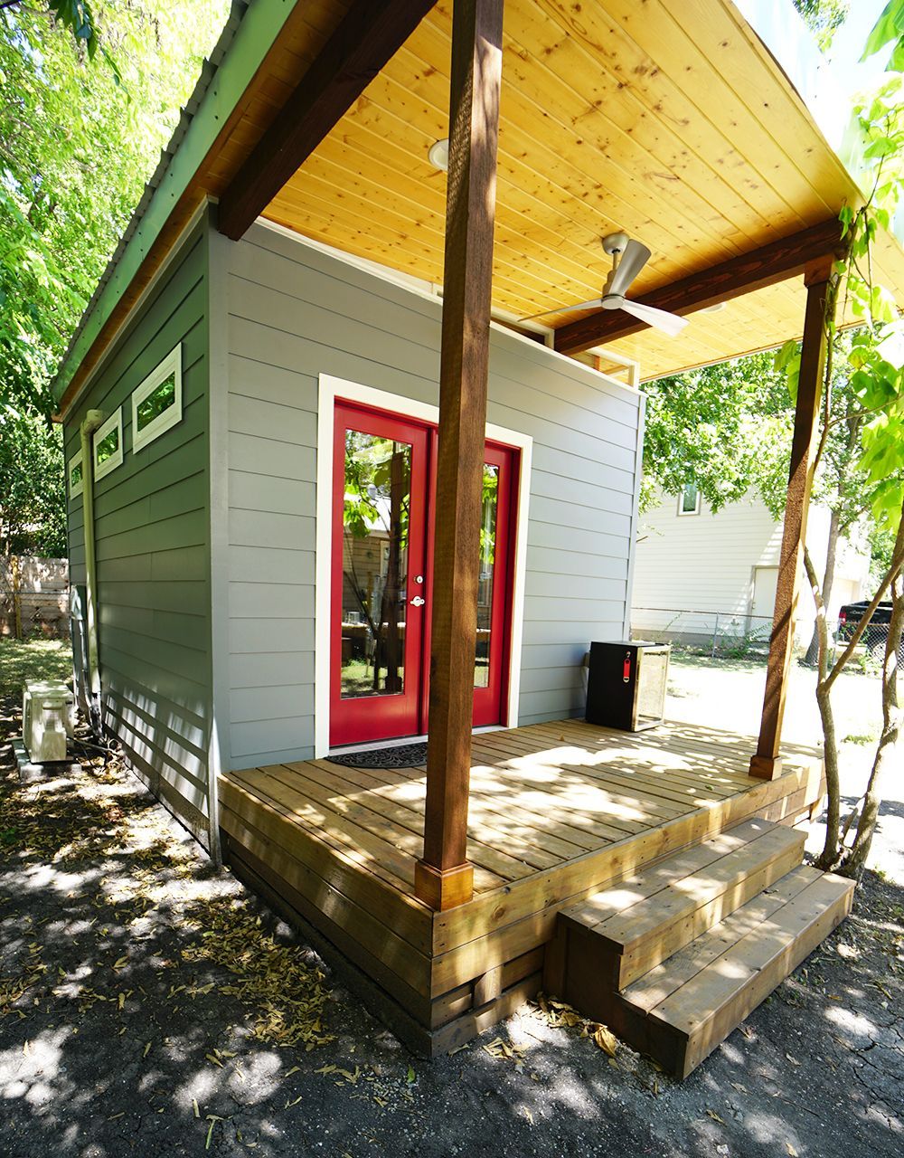 Small gray building with a red door and a wooden porch.