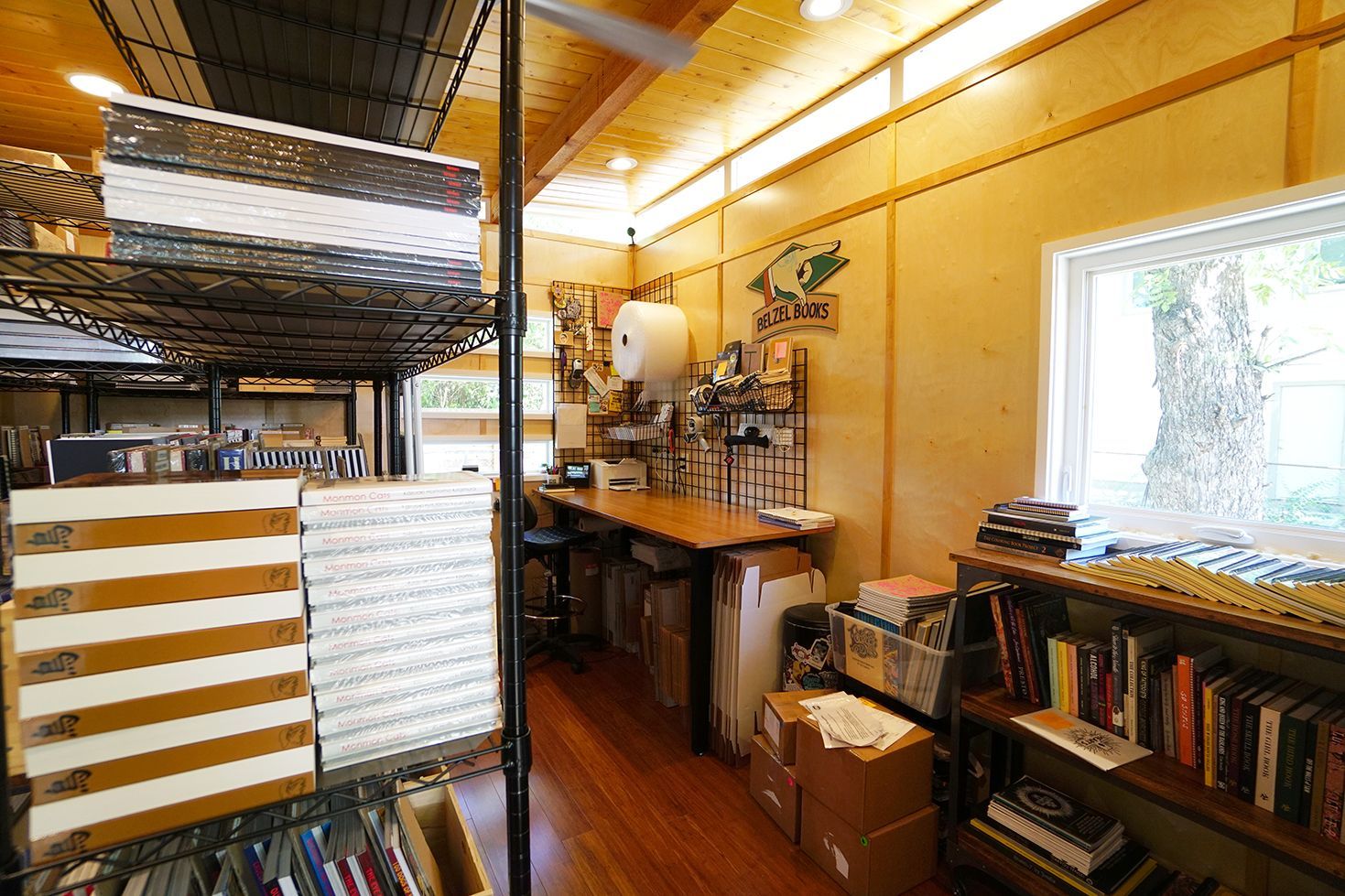 Interior of a craft room with shelves, desk, and window. Boxes, books, and art supplies are visible.