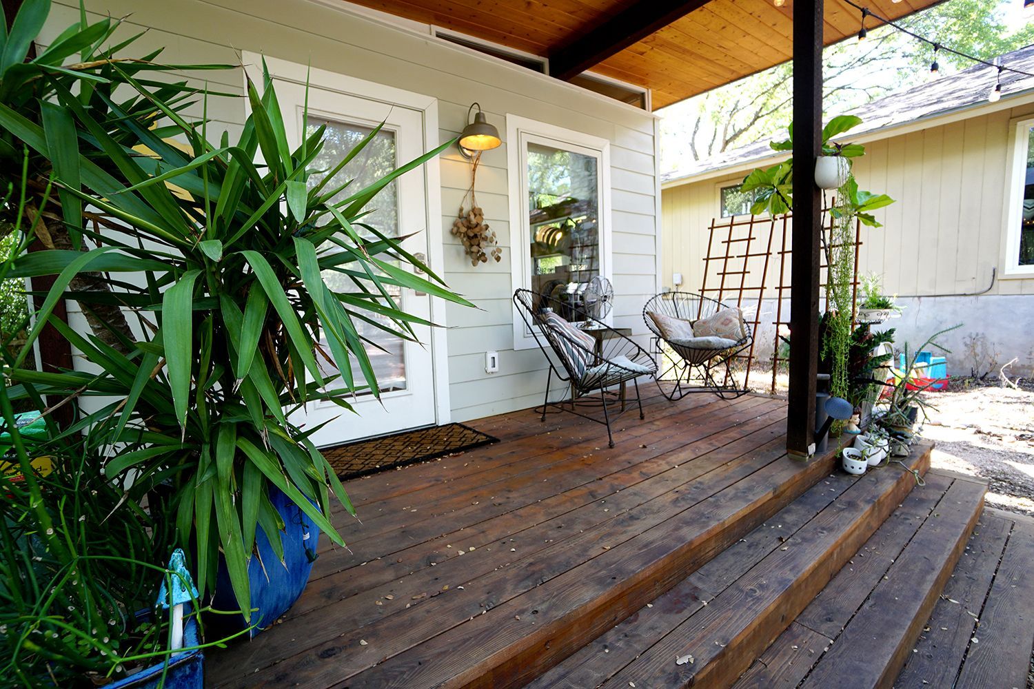 Wooden porch with seating and potted plants in front of a light gray house.