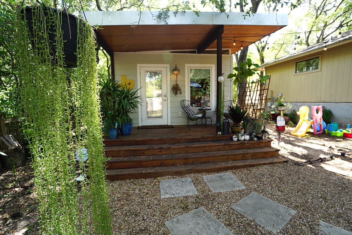 Small backyard structure with a covered porch, wooden steps, and a gravel yard.