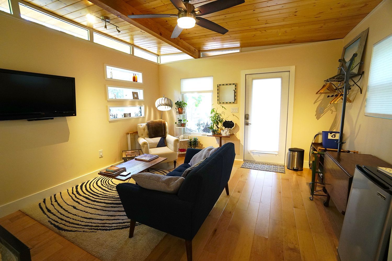 Cozy living room with a blue sofa, TV, and wooden ceiling. Sunlight streams in from windows.