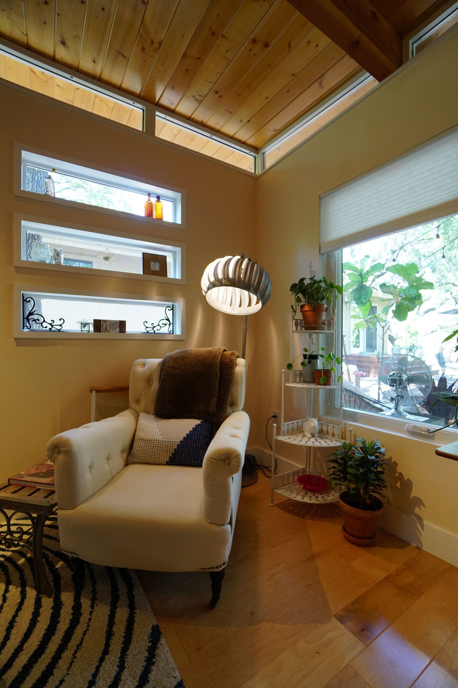 Cozy living room with cream armchair, window, shelving with plants, and wood flooring.