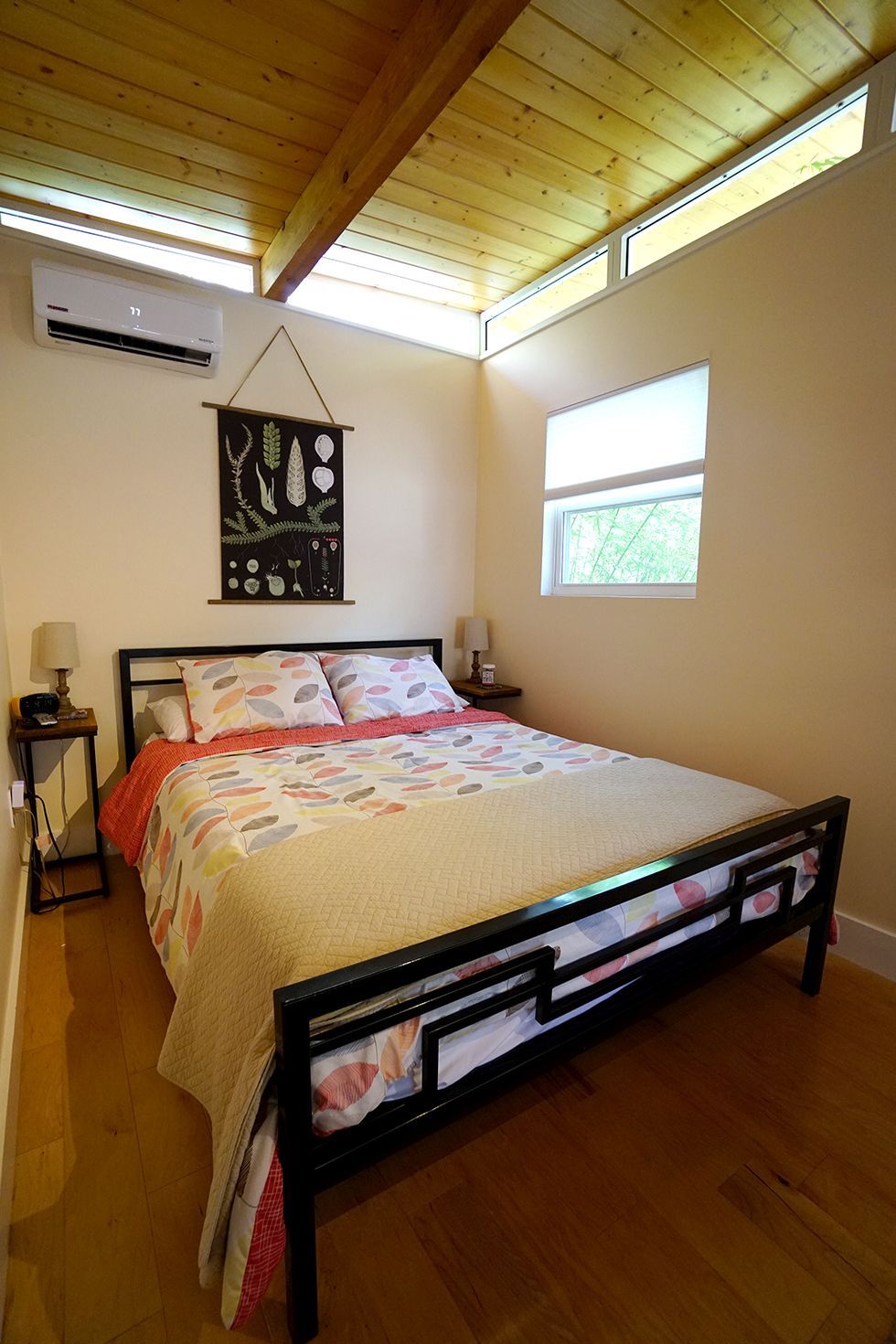 Bedroom with a black metal bed, light wood floors, and a light-colored quilt, near a window.