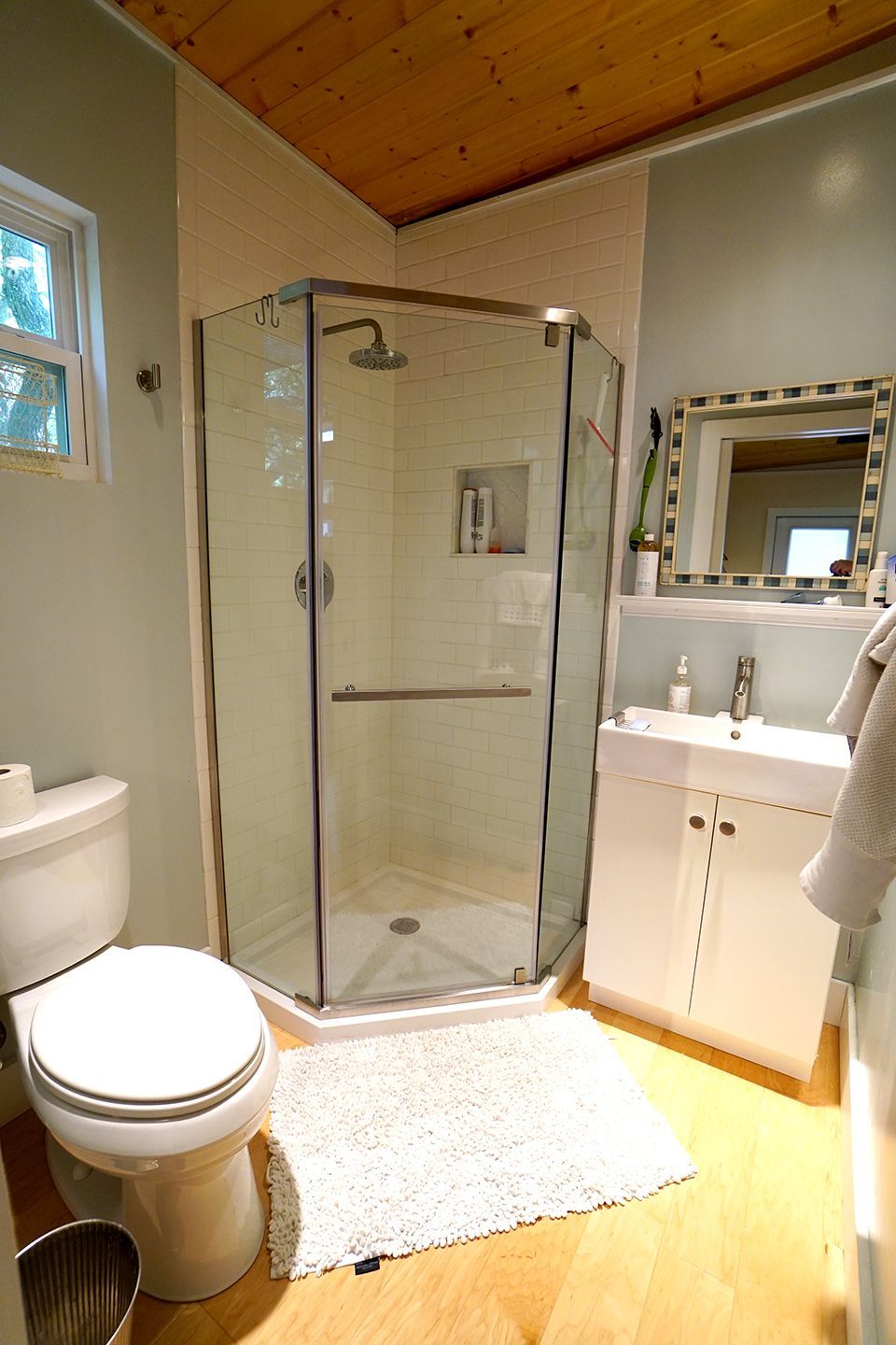 Bathroom with glass shower, white toilet, vanity, and a wooden floor.