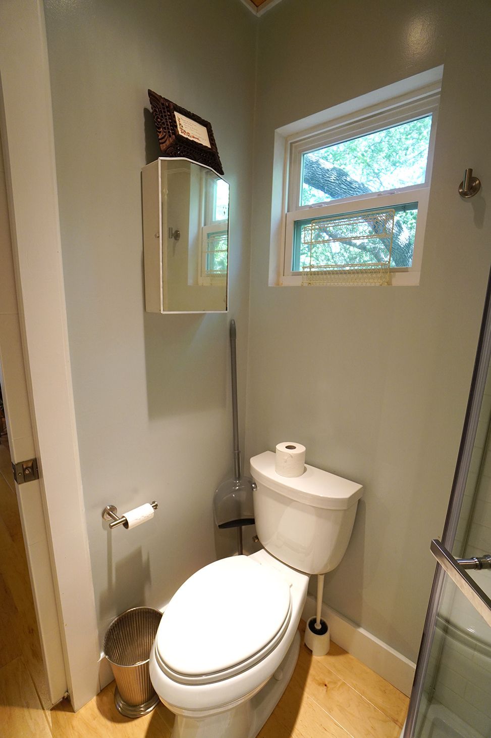 Small bathroom with toilet, window, and cabinet. Pale green walls, light wood floor.