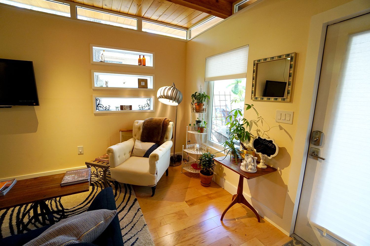 Cozy living room with cream walls, hardwood floors, a white armchair, and a small side table next to the entrance.