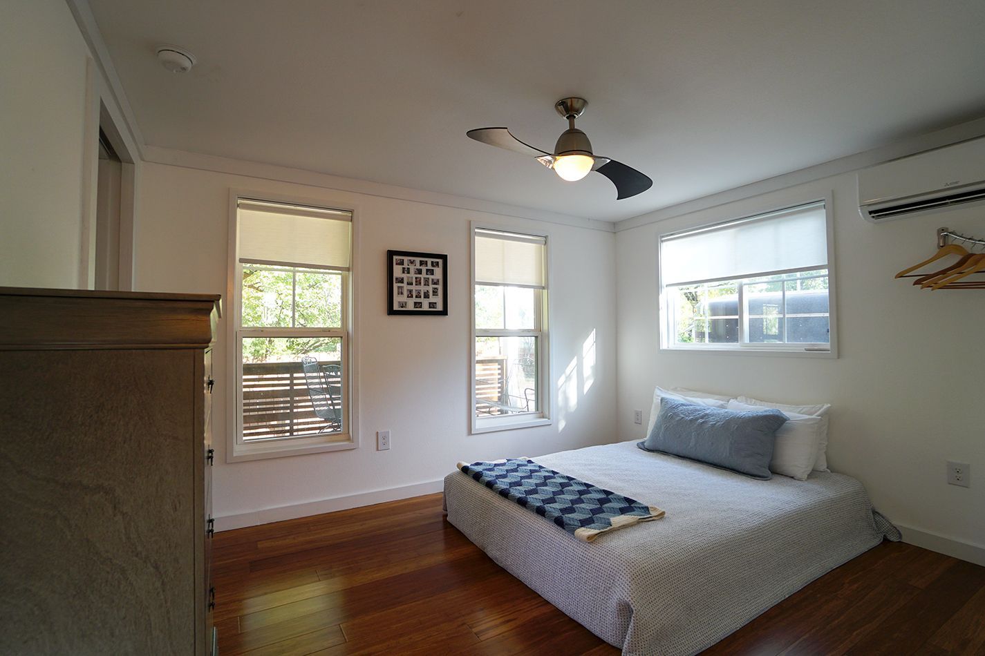 Bedroom with hardwood floor, bed, windows with blinds, ceiling fan, and dresser.