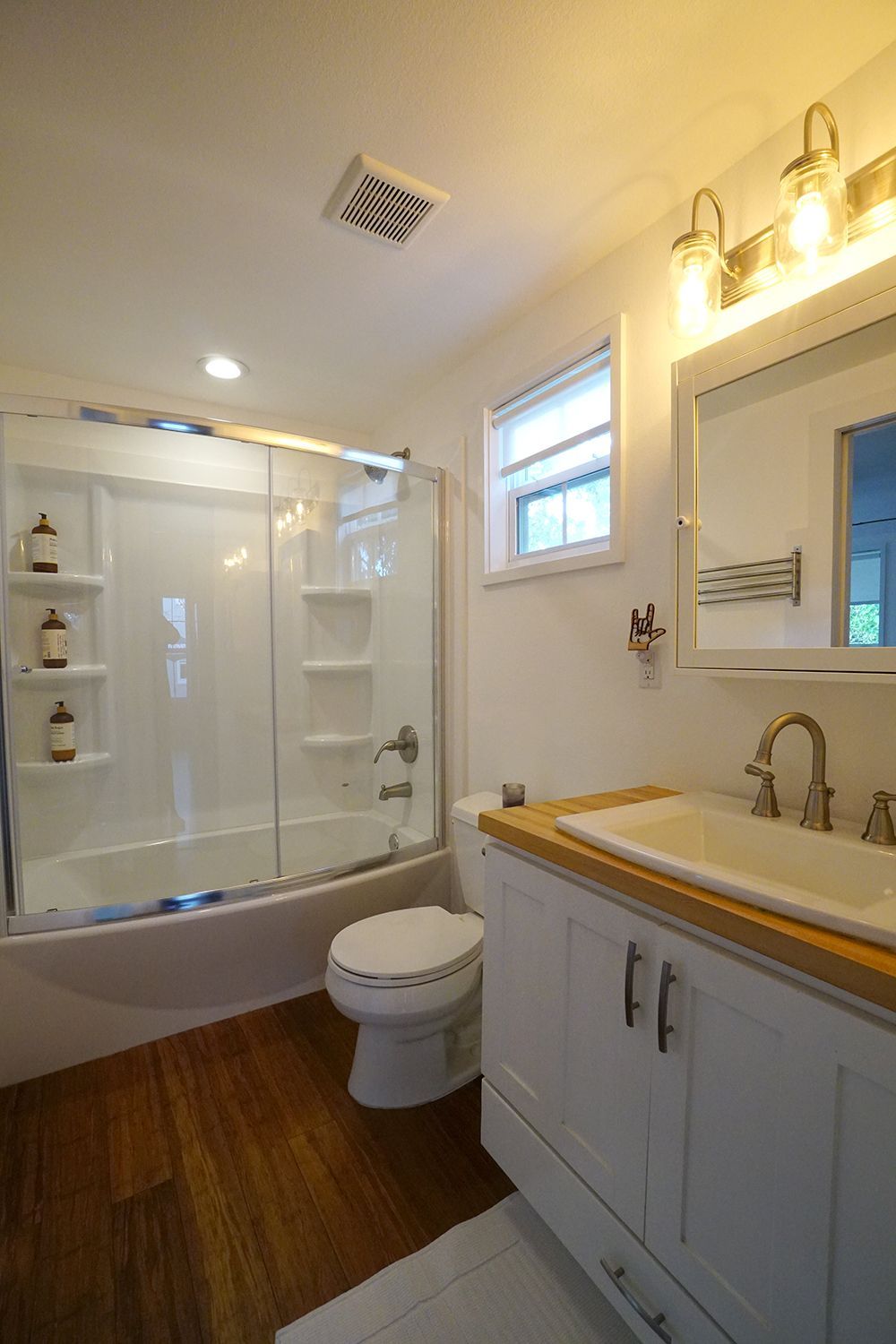 Bathroom with white fixtures, wooden floor, glass shower, and vanity.