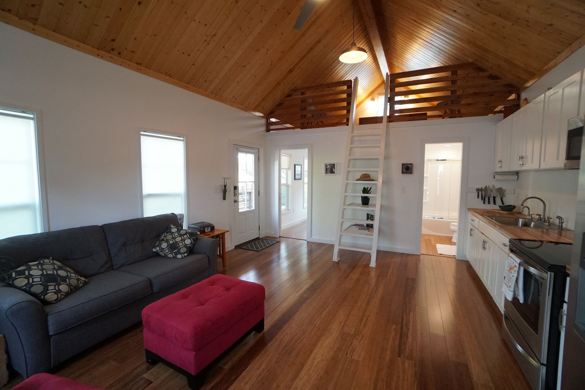 Cozy, open-concept living space with wooden floor, couch, kitchen, and loft area.