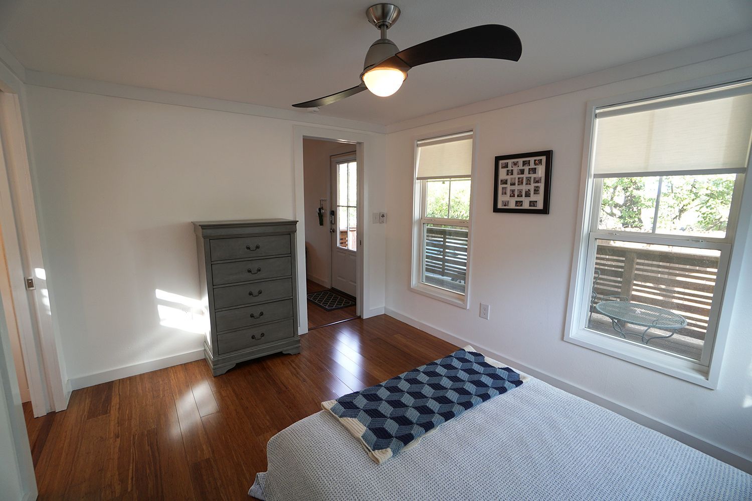 Bedroom with hardwood floors, a gray dresser, windows, and a ceiling fan.
