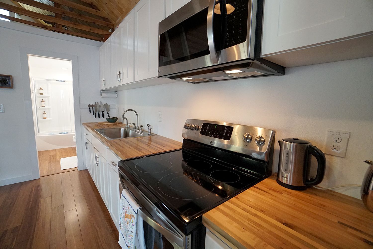 A small kitchen with a stove, microwave, and sink, light wood counters and white cabinets.