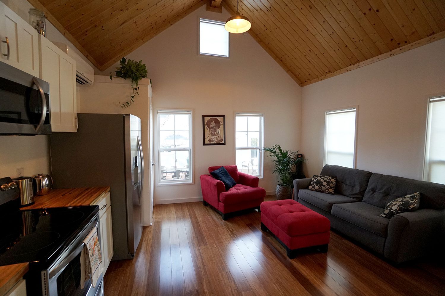 Living room with wood floors and vaulted ceiling.  Red sofa and ottoman, grey couch, kitchen on the left.