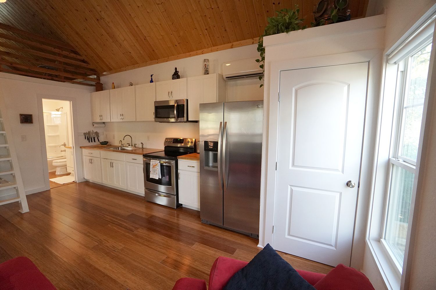 Kitchen with stainless steel appliances, white cabinets, and wooden floors.  Doorway to bathroom on left.