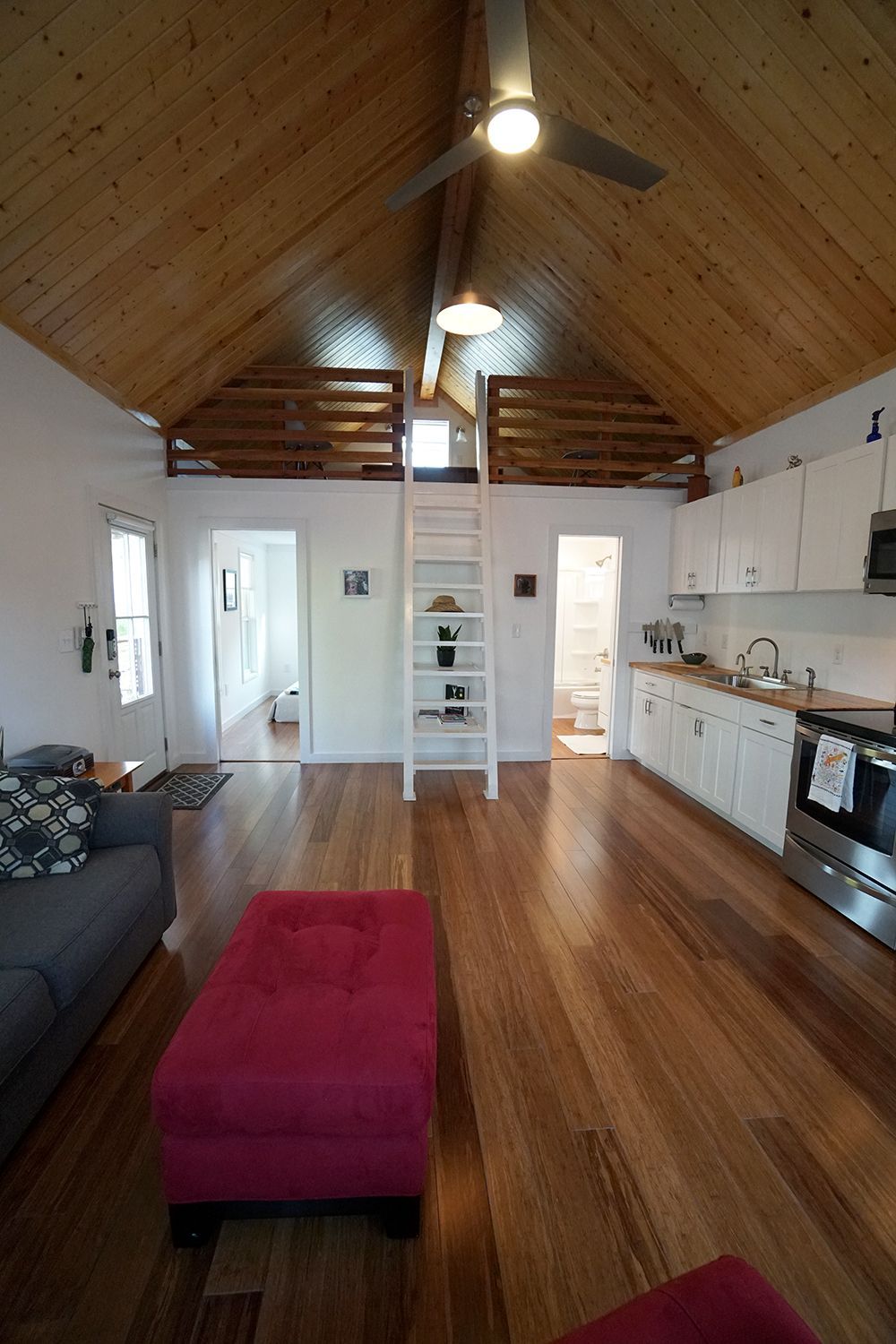 Interior of a small home with wooden floors, white walls, and a loft. Kitchen and living area visible.
