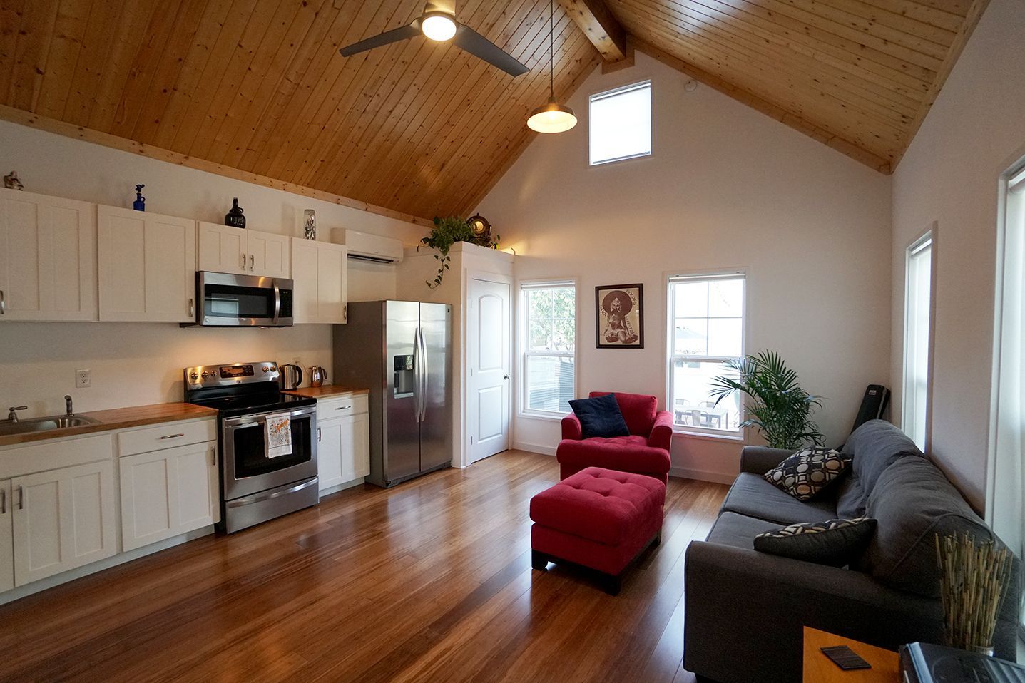Living space with kitchen, couch, red chair, and wooden ceiling.