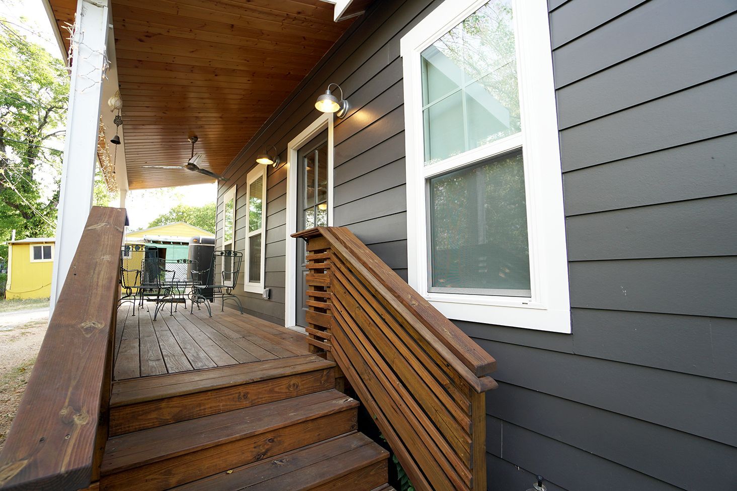 Wooden porch with steps leading up to a gray-sided house with white-framed windows.