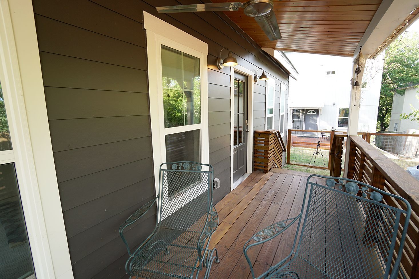 A wooden deck with metal chairs and a view of a house. Brown siding, white window trim.