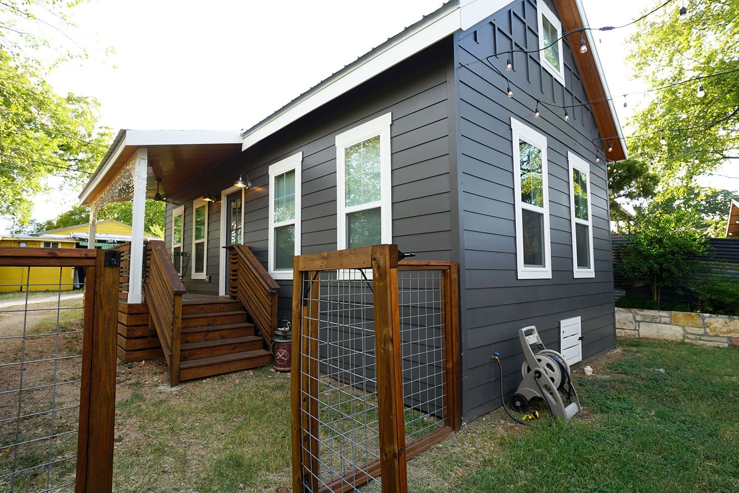 Dark gray house with white trim, porch, and wooden fence.