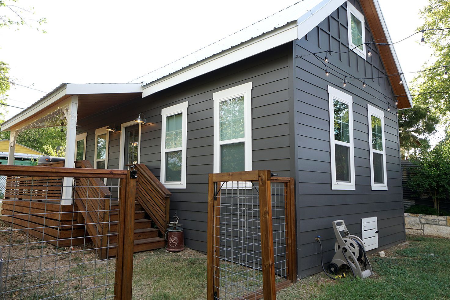 Gray house with white-trimmed windows and a covered porch, set on a grassy yard with a wooden fence.