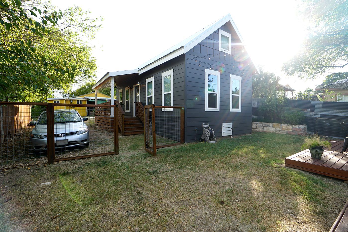 Black house with white trim, fenced yard, and small car parked in front.