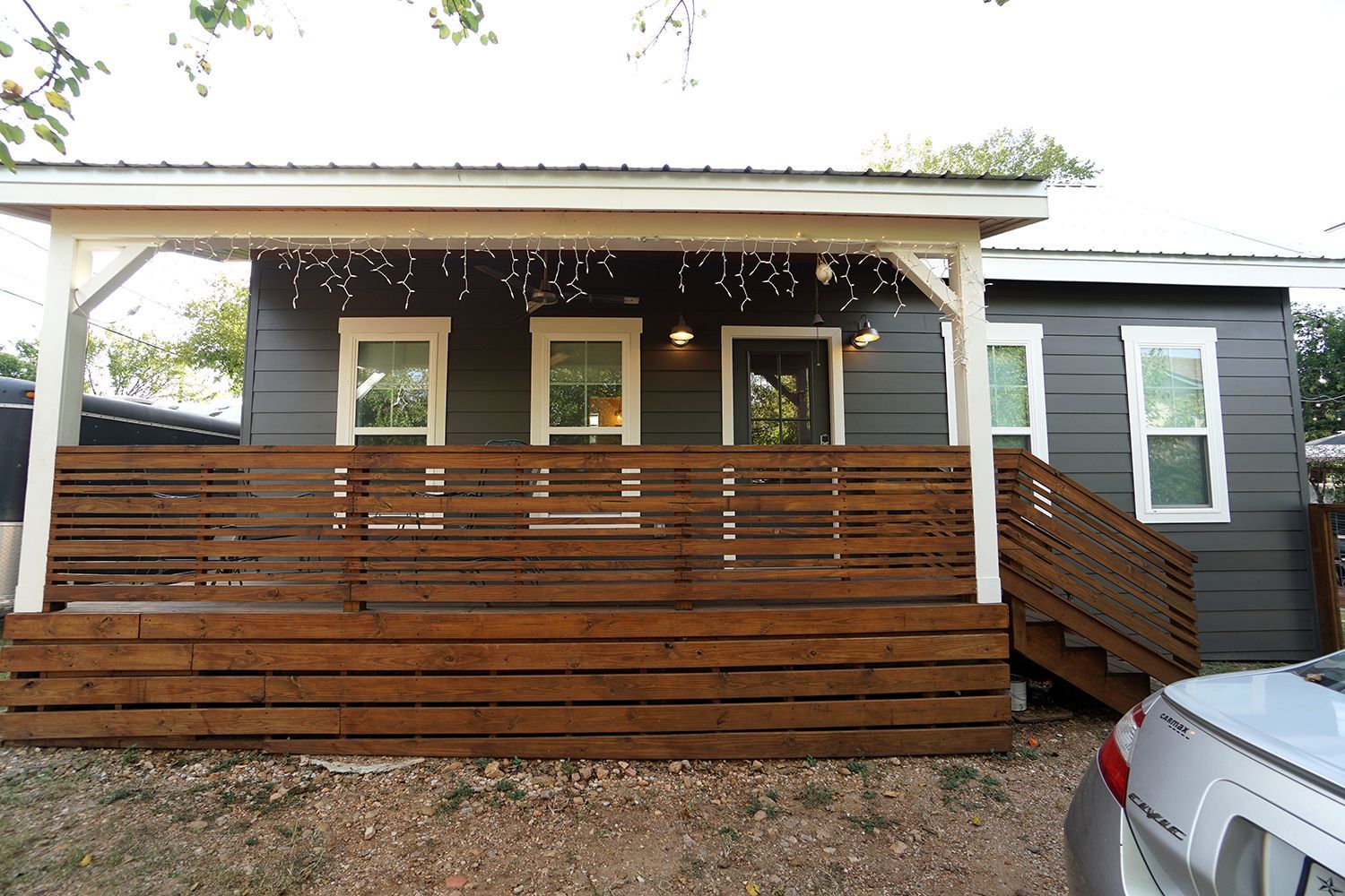 Gray house with wooden porch and brown horizontal railing, white trim.