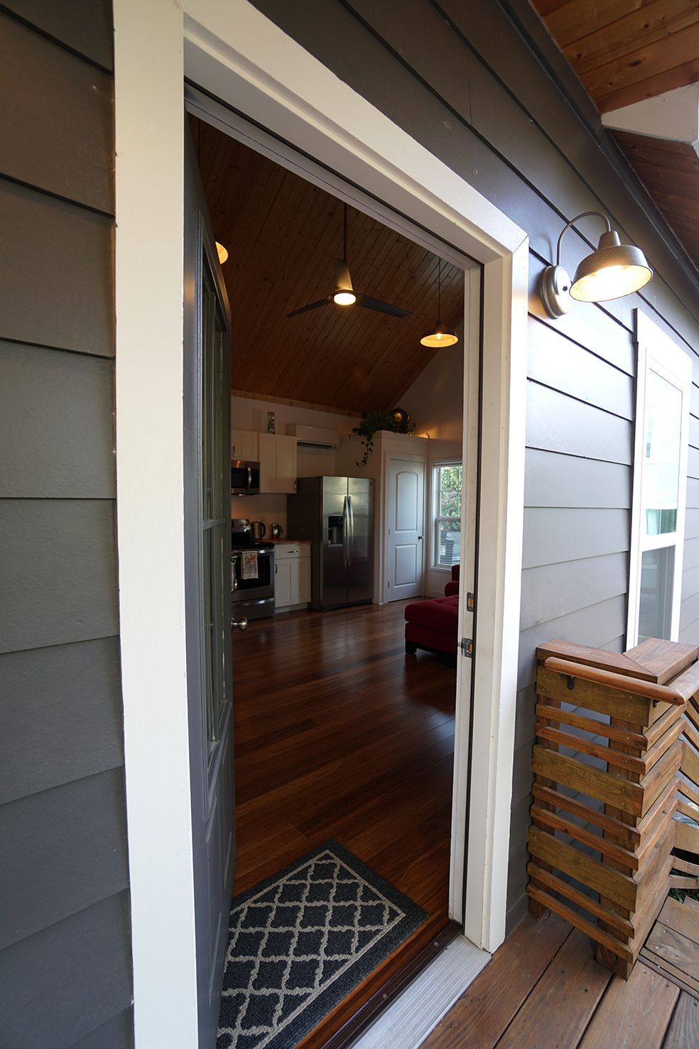 Open doorway into a home with hardwood floors. Exterior is gray siding, interior includes kitchen and living space.